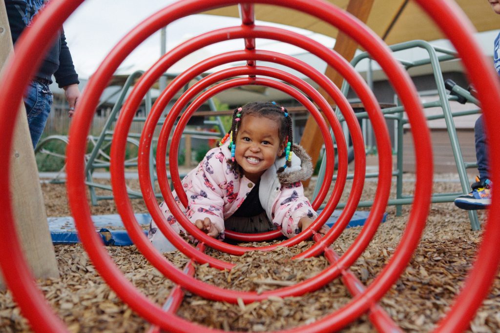 alt: "a girl crawling in a circular metal structure practicing Risky Play." 