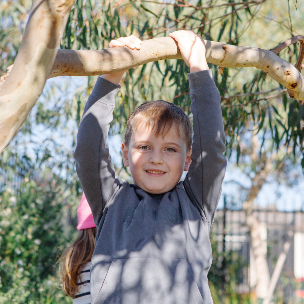 alt="Four-year-old child hanging from a tree branch with both hands"